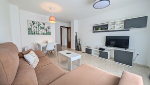 Ein modernes Wohnzimmer mit einer Couch, einem Esstisch, einem Fernseher und einem Deckenventilator.