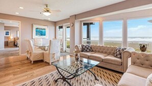 Un salón amplio con una mesa de centro de vidrio, sofás color beige y vista al océano.