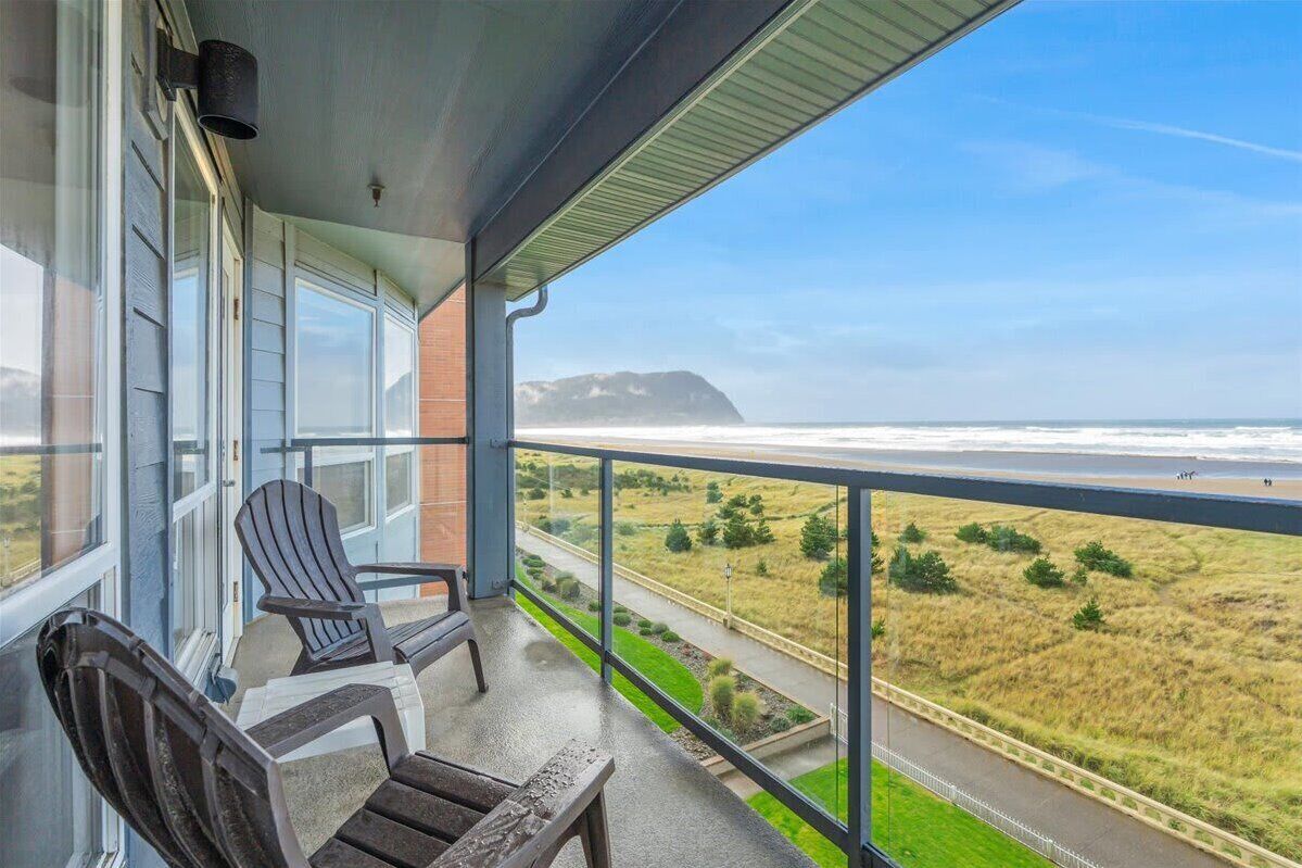 A balcony with chairs, a view of the ocean, and a distant mountain.