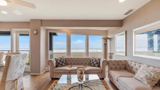 Un salón con un sofá color beige, una mesa de centro de vidrio y vista a la playa.