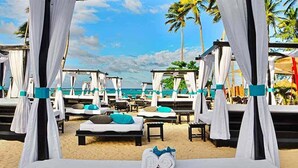 Quarto de hotel à beira-mar com cama, duas almofadas, toalha e vista para o oceano e palmeiras.