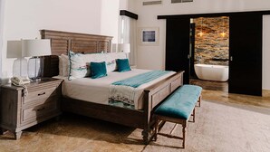 Quarto com cama, mesas de cabeceira, um banquinho, uma banheira e vista para uma parede de pedra.