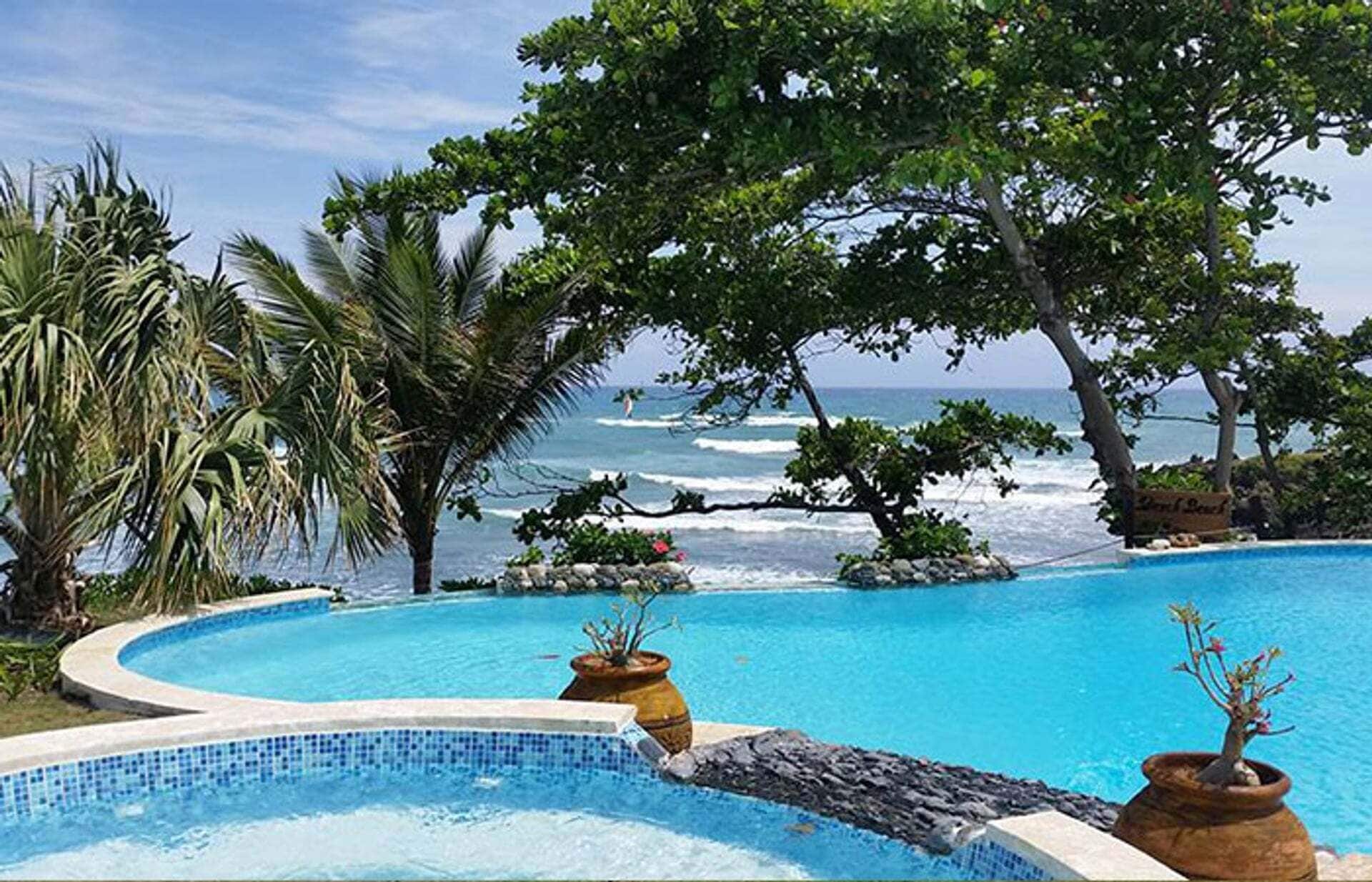 A pool with a curved edge, surrounded by tropical vegetation and overlooking the ocean.