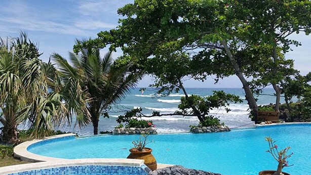 Piscina com borda curva, rodeada por vegetação tropical e vista para o oceano.