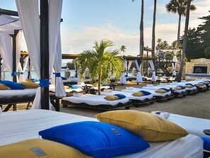 A beachside hotel with rows of sunbeds, palm trees, and a clear sky. - Luxury 3BR Villa | Private Chef, Golf Cart & Pool | VIP Beach Access (Cabarete)