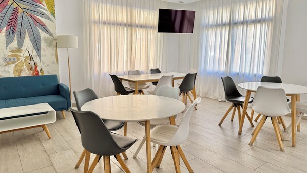 A modern meeting room with round tables, chairs, a blue sofa, and a flat-screen TV. - Hotel Celymar (Benidorm)