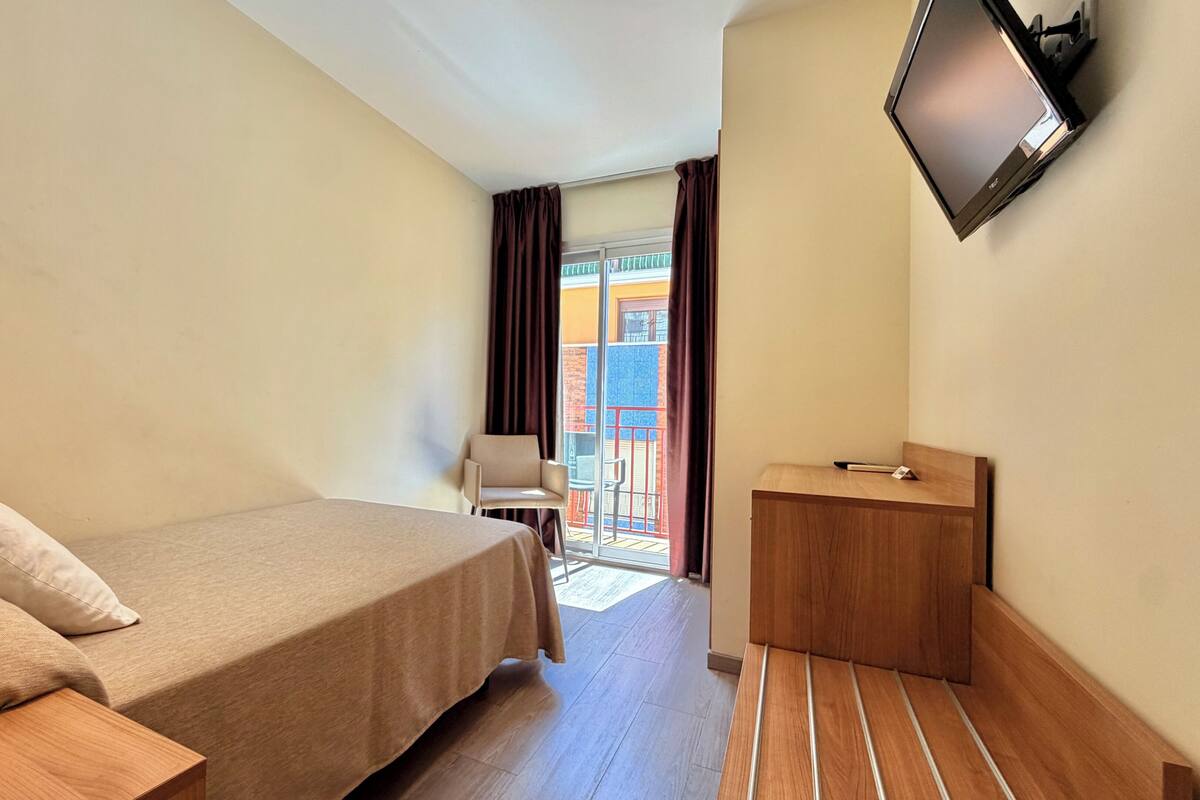 Une chambre d’hôtel avec un lit, un bureau, une chaise, une télévision et un balcon avec vue.