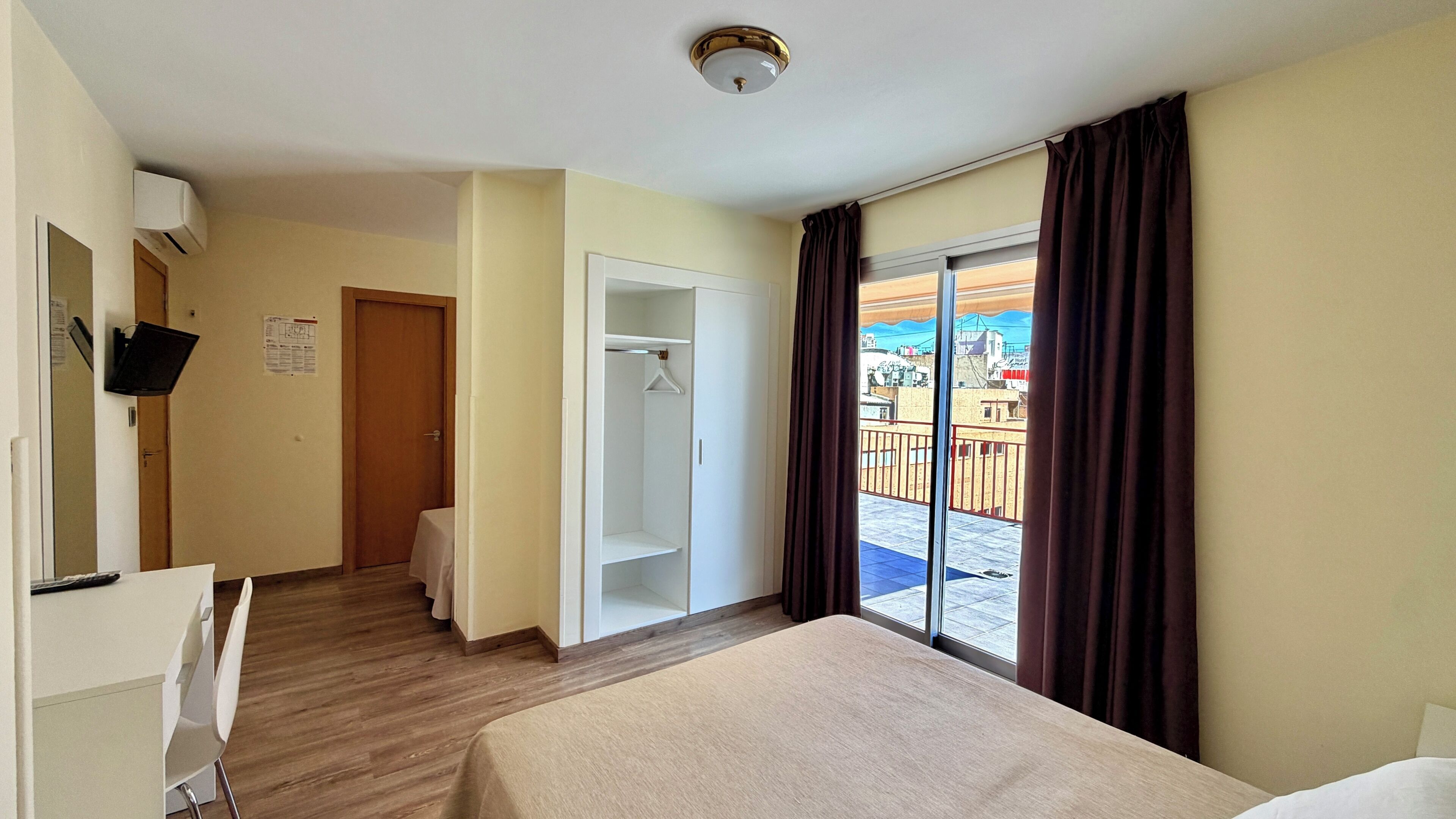Een hotelkamer met een bed, een kledingkast, een bureau en een raam met gordijnen.