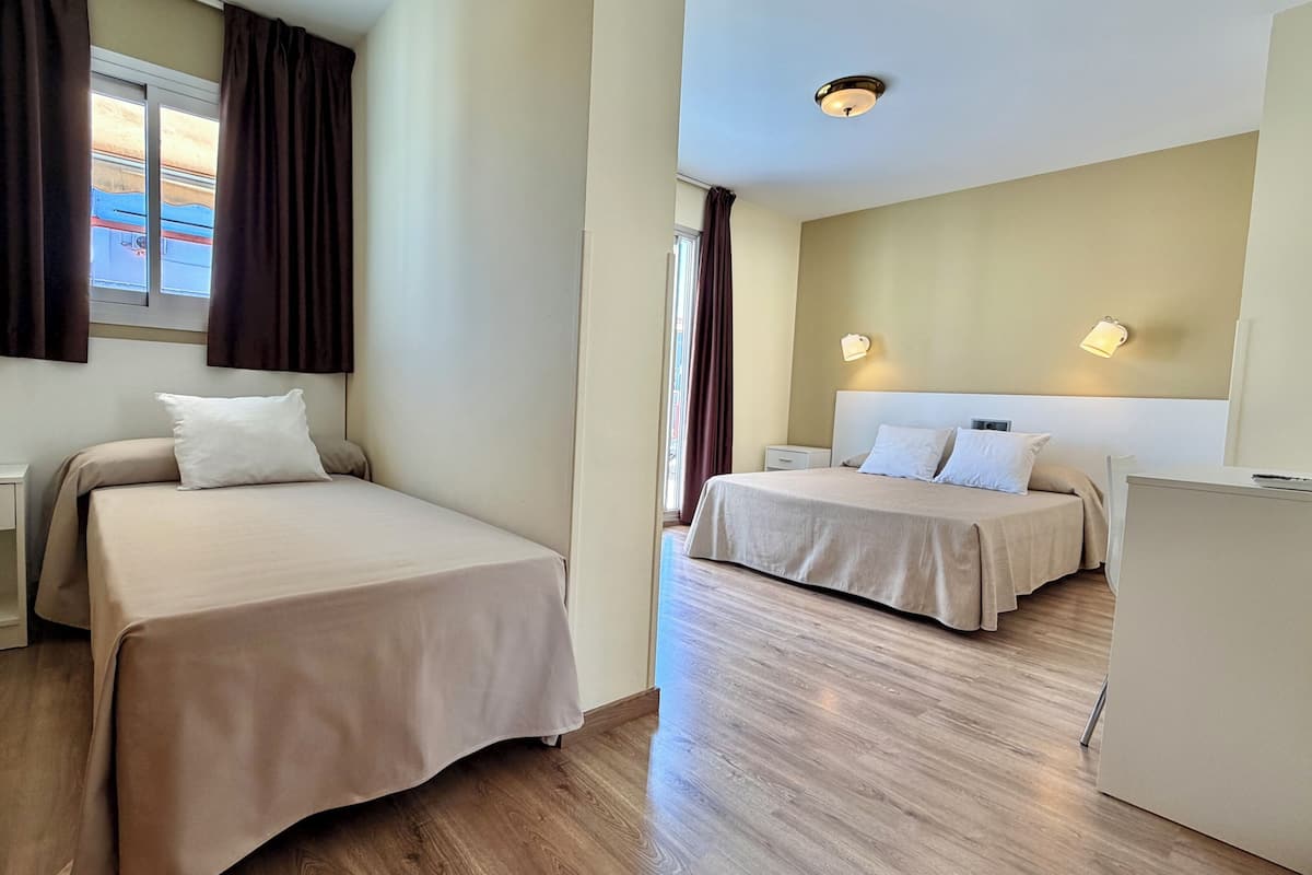 Une chambre d’hôtel avec deux lits, un bureau, un petit réfrigérateur et une fenêtre avec des rideaux.