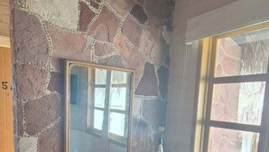 A room with a stone wall, a wooden desk with a chair, a large mirror, and a window with a view. - SS 5A Cabaña rustica frente al malecón de La Paz (La Paz)