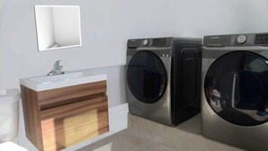 Ein Badezimmer mit einem Holzkosmetikschrank, einem Waschbecken und zwei Waschmaschinen mit Frontlader.