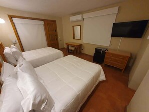 Camera d'albergo con due letti, una scrivania, una sedia, una televisione e un armadio.