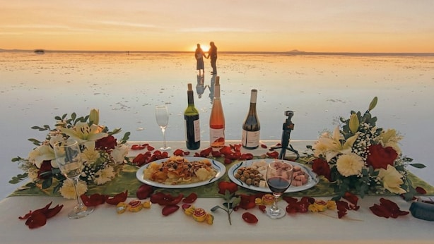 Une table dressée avec de la nourriture et des boissons sur une plage, au coucher du soleil.