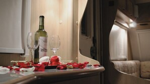 Un coin repas avec une table dressée pour deux personnes, agrémentée d’une bouteille de vin, de deux verres à vin et de pétales de roses rouges.