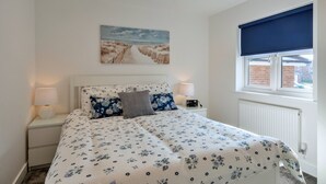 Ein Schlafzimmer mit Bett, Nachttisch, Lampe, Fenster mit Jalousie und einem Bild an der Wand.