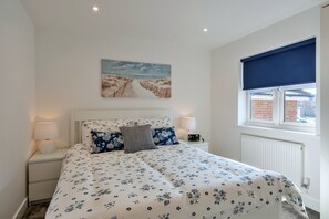 Ein Schlafzimmer mit Bett, Nachttisch, Lampe, Fenster mit Jalousie und einem Bild an der Wand.