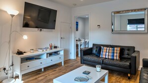 Ein modernes Wohnzimmer mit Flachbildfernseher, weißem Unterhaltungsschrank, schwarzem Ledersofa und einem Couchtisch.