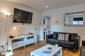 Ein modernes Wohnzimmer mit Flachbildfernseher, weißem Unterhaltungsschrank, schwarzem Ledersofa und einem Couchtisch.