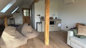 A modern interior with exposed wooden beams, a kitchenette, and a seating area with bean bags. - The Loft – 1 bed space with gated parking (Binfield Heath)
