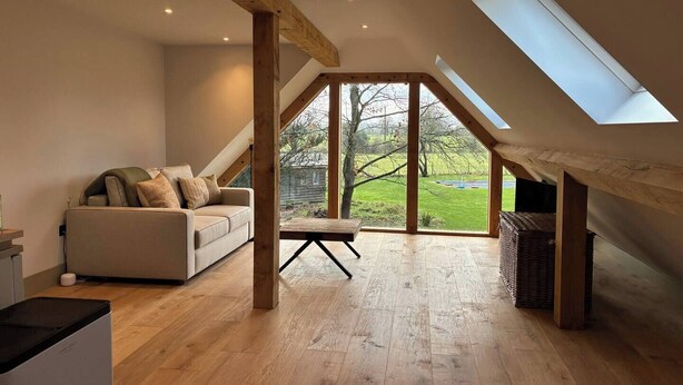 A loft bedroom with a sloped ceiling, a wooden floor, a sofa, and a view of the outdoors. - The Loft – 1 bed space with gated parking (Binfield Heath)