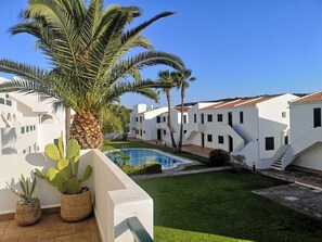 A courtyard with a swimming pool, palm trees, and white buildings with red-tiled roofs. - Golf & Beach Holiday Home, Menorca (Son Parc)
