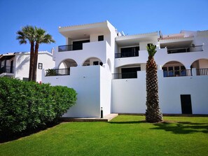 A multi-story white building with balconies, a palm tree, and a well-maintained lawn. - Golf & Beach Holiday Home, Menorca (Son Parc)