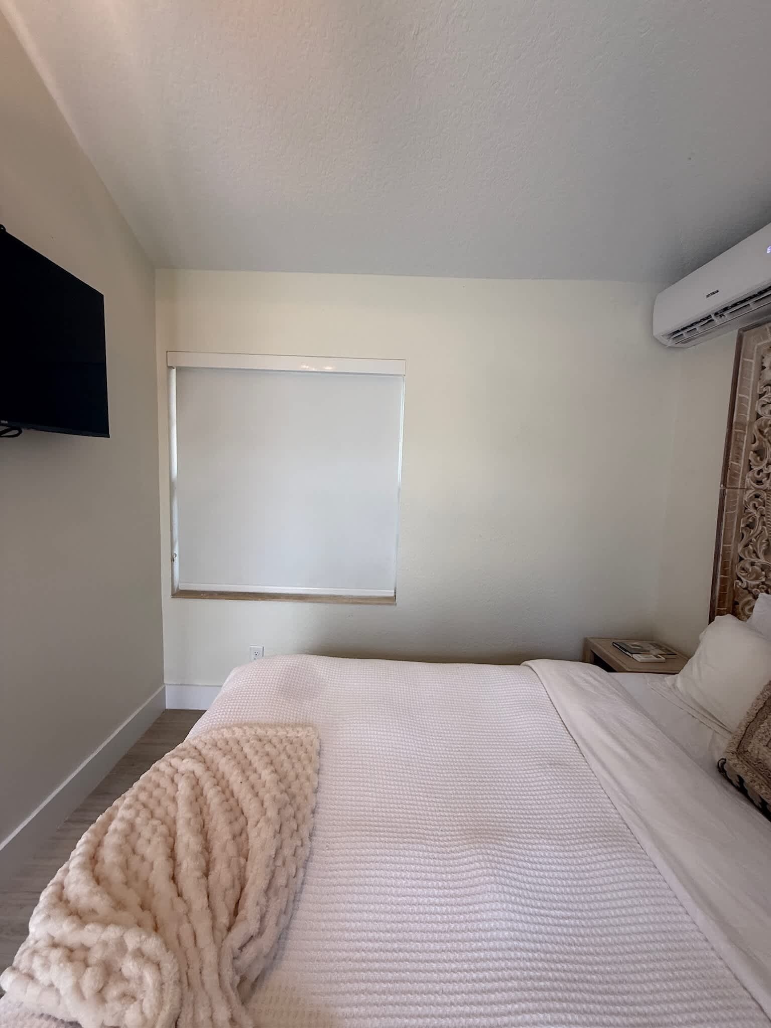 A bedroom with a bed, a television, an air conditioning unit, and a window.