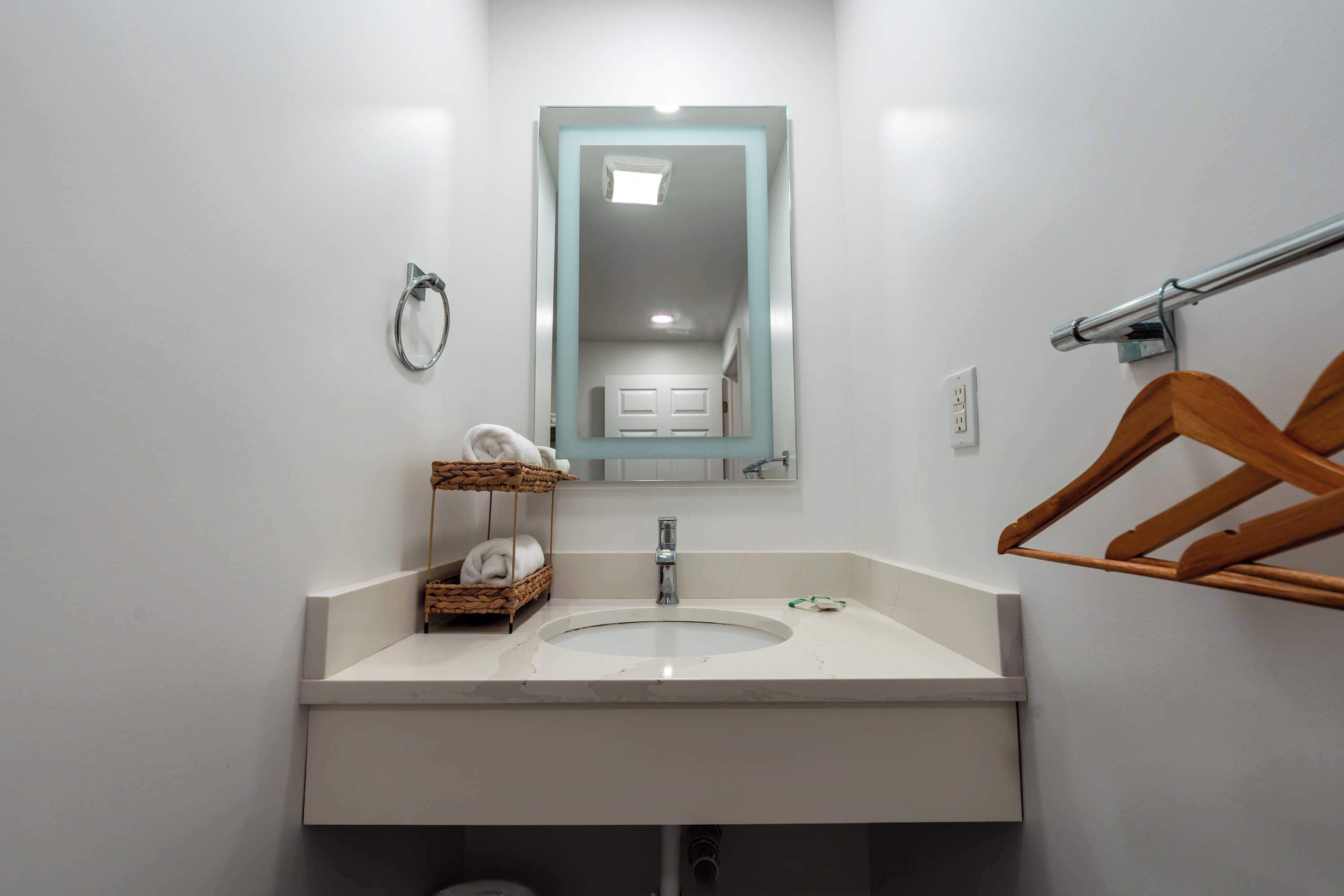 Un bagno con un lavandino bianco, uno specchio, un portascopevoli e un appendiabiti in legno.