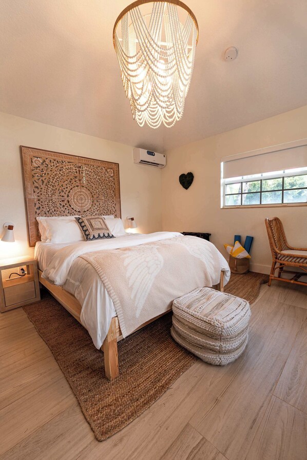 A bedroom with a large bed, a decorative ceiling light, a window, and a chair.