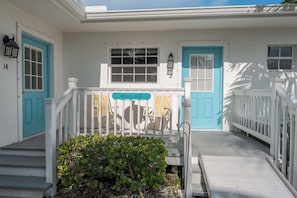 A white building with blue doors and windows, a porch with a sign reading 'Beach Bungalow,' and a small garden area.