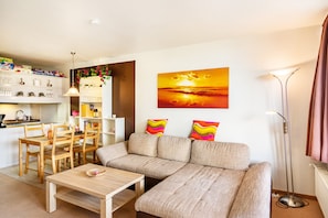 A modern living room with a sofa, dining table, and chairs. There is a painting on the wall and a floor lamp. - Cozy Holiday Apartment in the Harz with Shared Pool and Balcony (Braunlage)