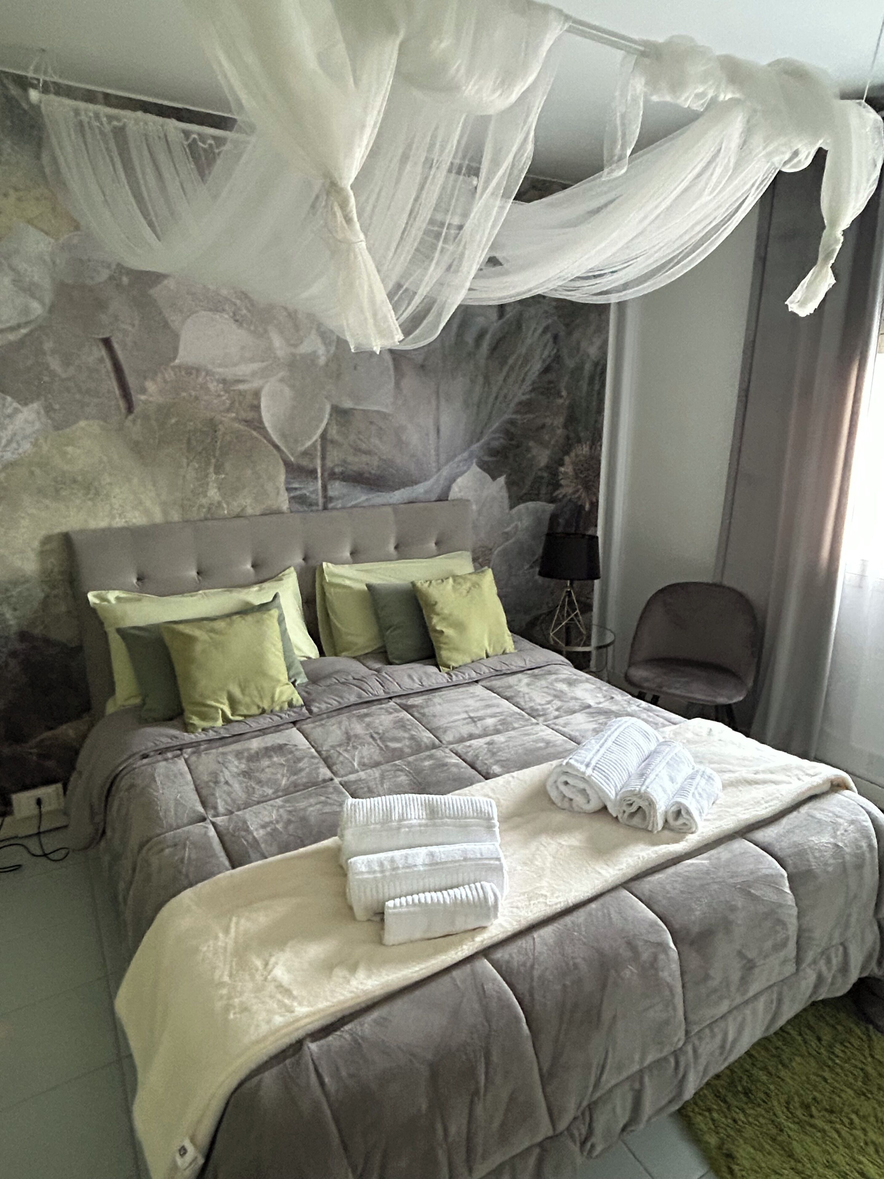 A bedroom with a bed, a nightstand, a chair, and a stone wall.