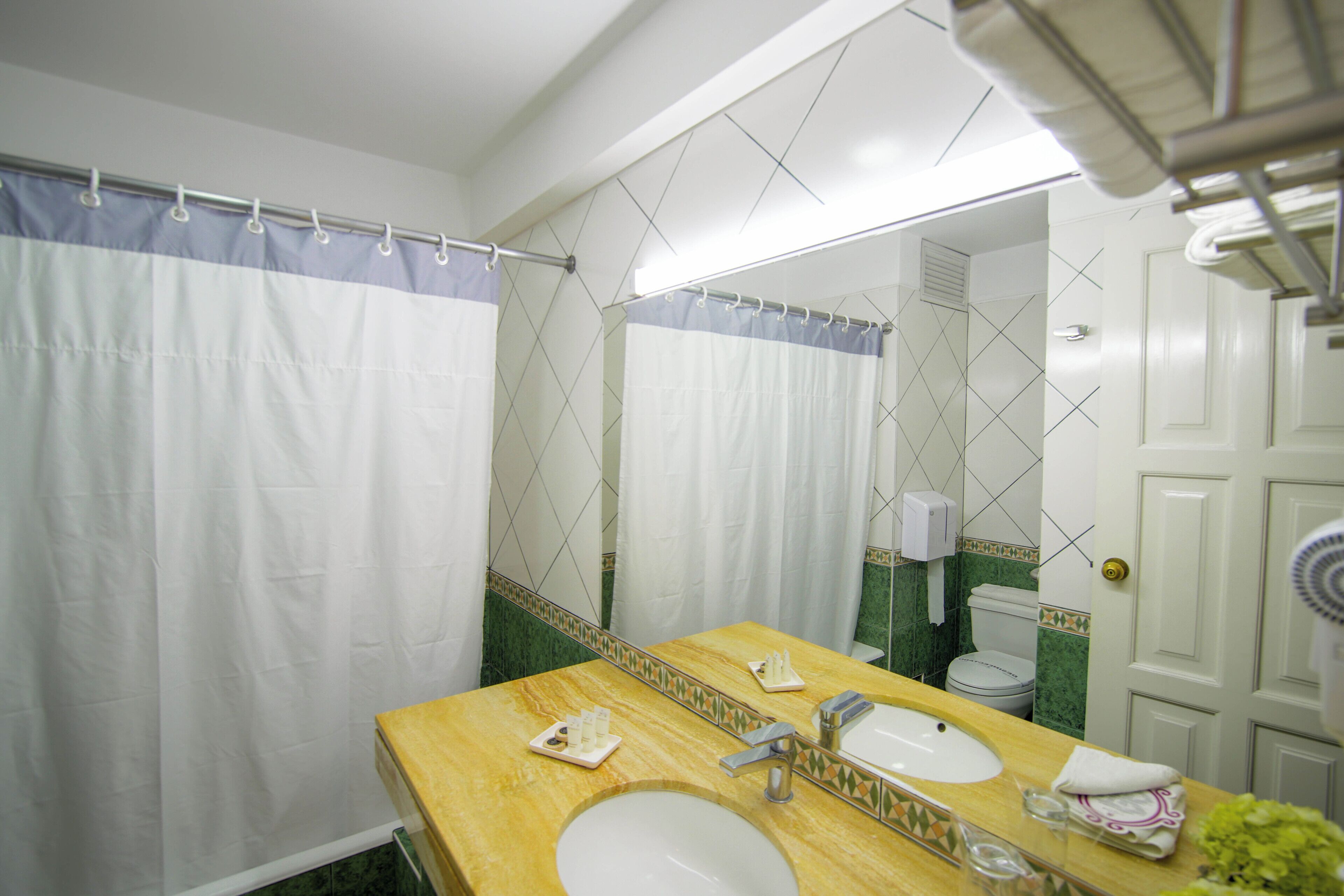 Un baño con tocador de madera, dos lavamanos, un espejo, cortina de ducha y un inodoro.
