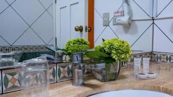 A bathroom with a white sink, two potted plants, a mirror, and a tiled wall.