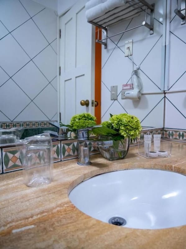A bathroom with a white sink, two potted plants, a mirror, and a tiled wall. - Britania San Borja (Lima)