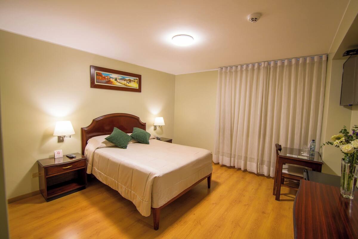 A hotel room with a bed, bedside lamps, a desk, and a chair.