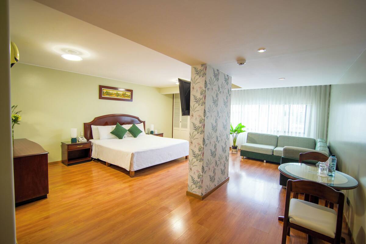 A hotel room with a bed, a sofa, a dining table, and a TV.