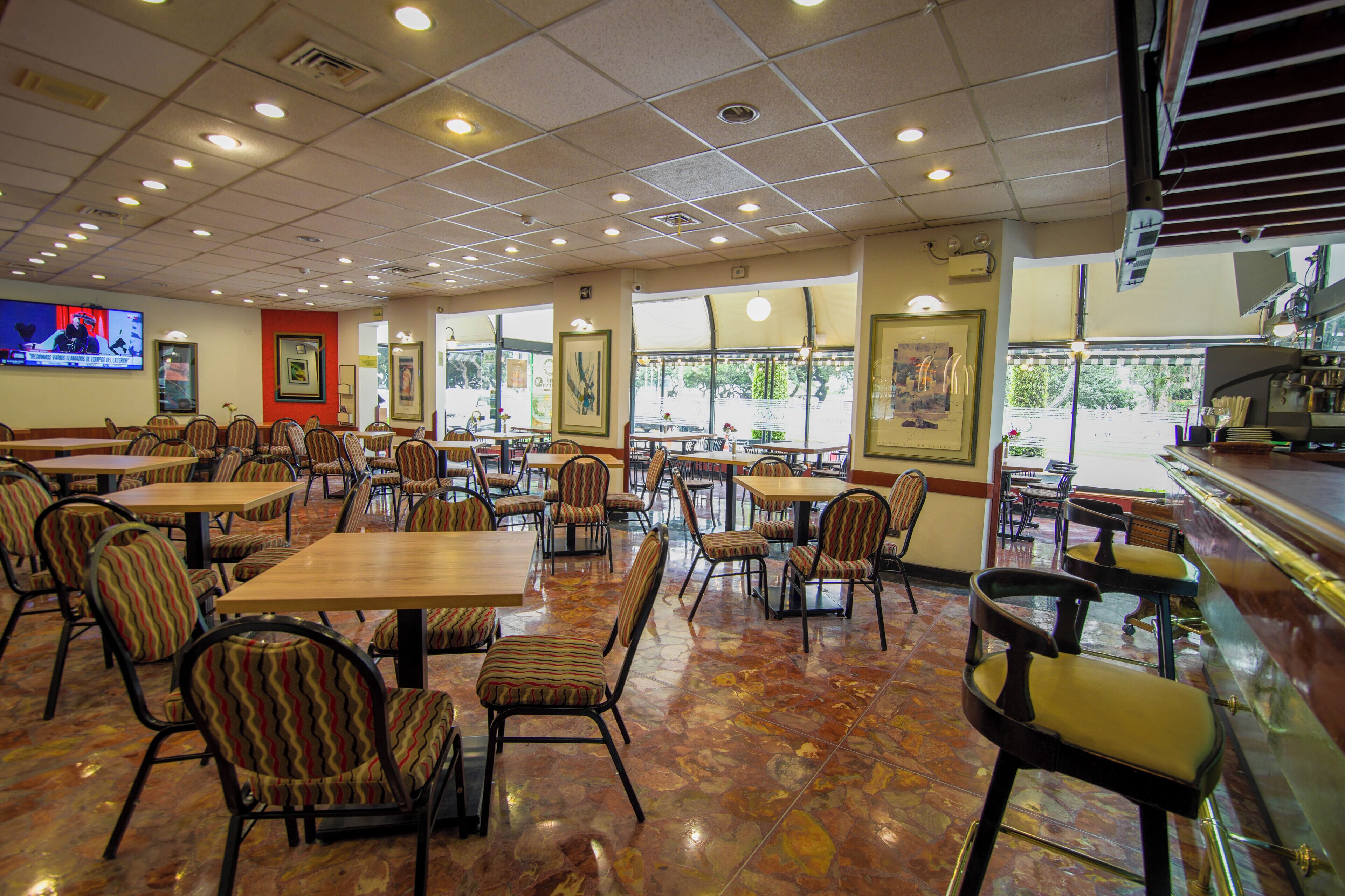 A restaurant interior with multiple tables and chairs, a bar area, and large windows.