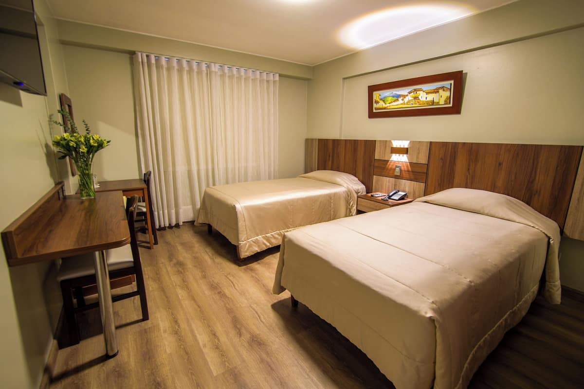 A hotel room with two beds, a desk, a chair, a lamp, and a painting on the wall.