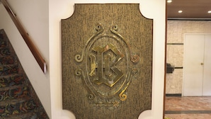 A wall-mounted emblem with a decorative letter 'K' and stars, a patterned carpet, and a marble floor. - Britania San Borja (Lima)