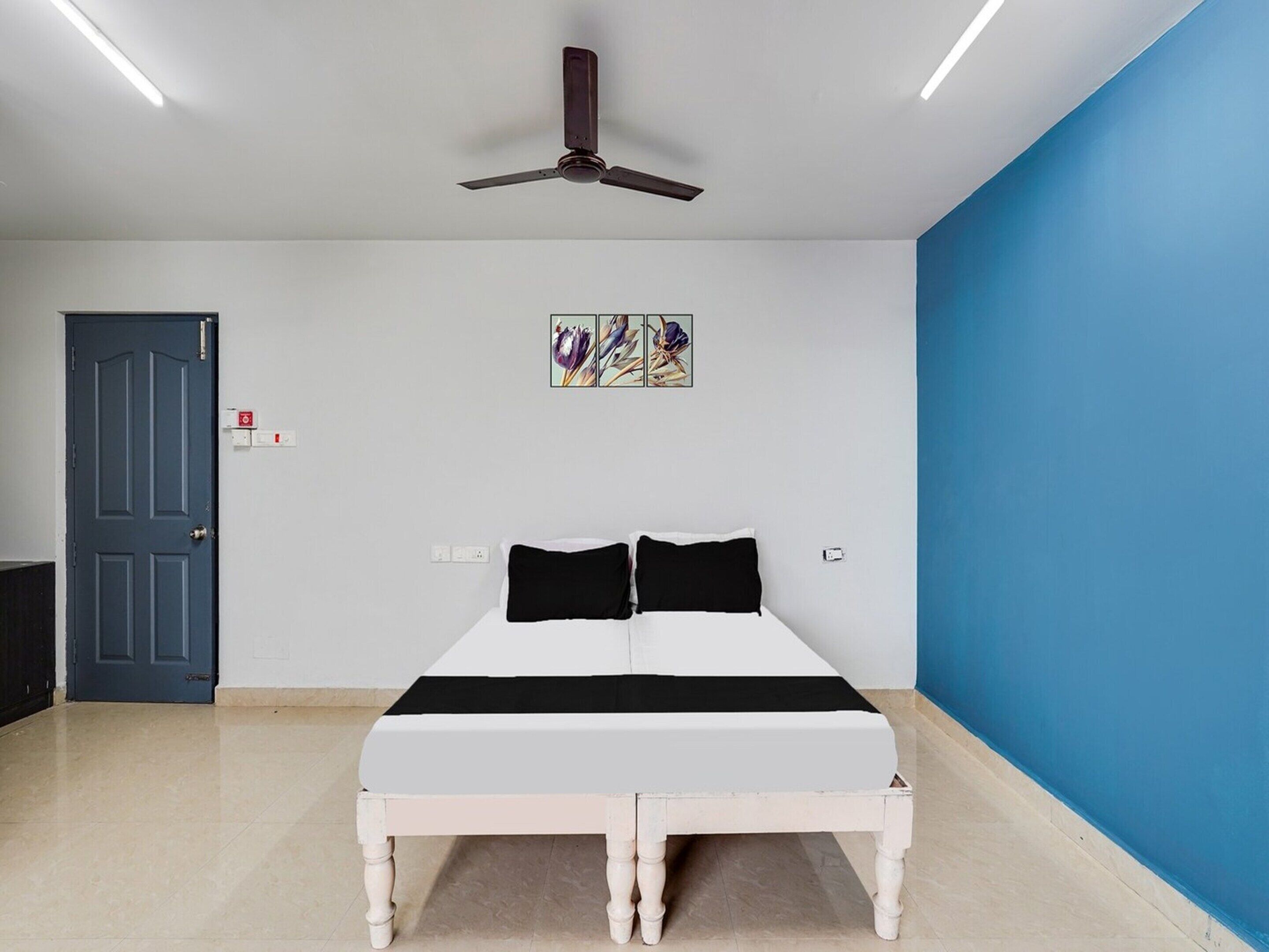 A bedroom with a bed, a ceiling fan, a door, and a wall with a painting.