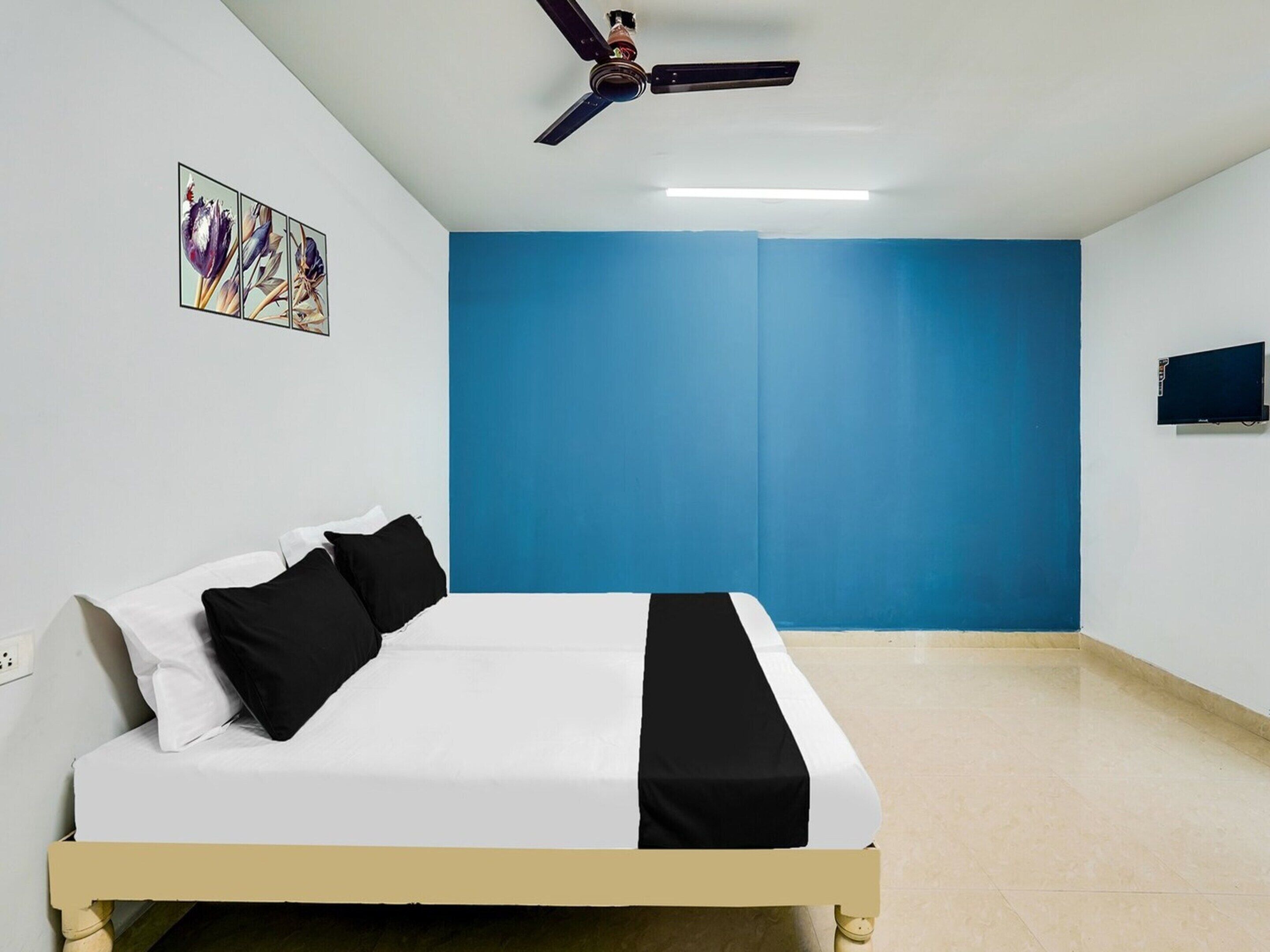 Ein Schlafzimmer mit einem Bett, einem Deckenventilator, einem an der Wand befestigten Fernseher und einem Gemälde.