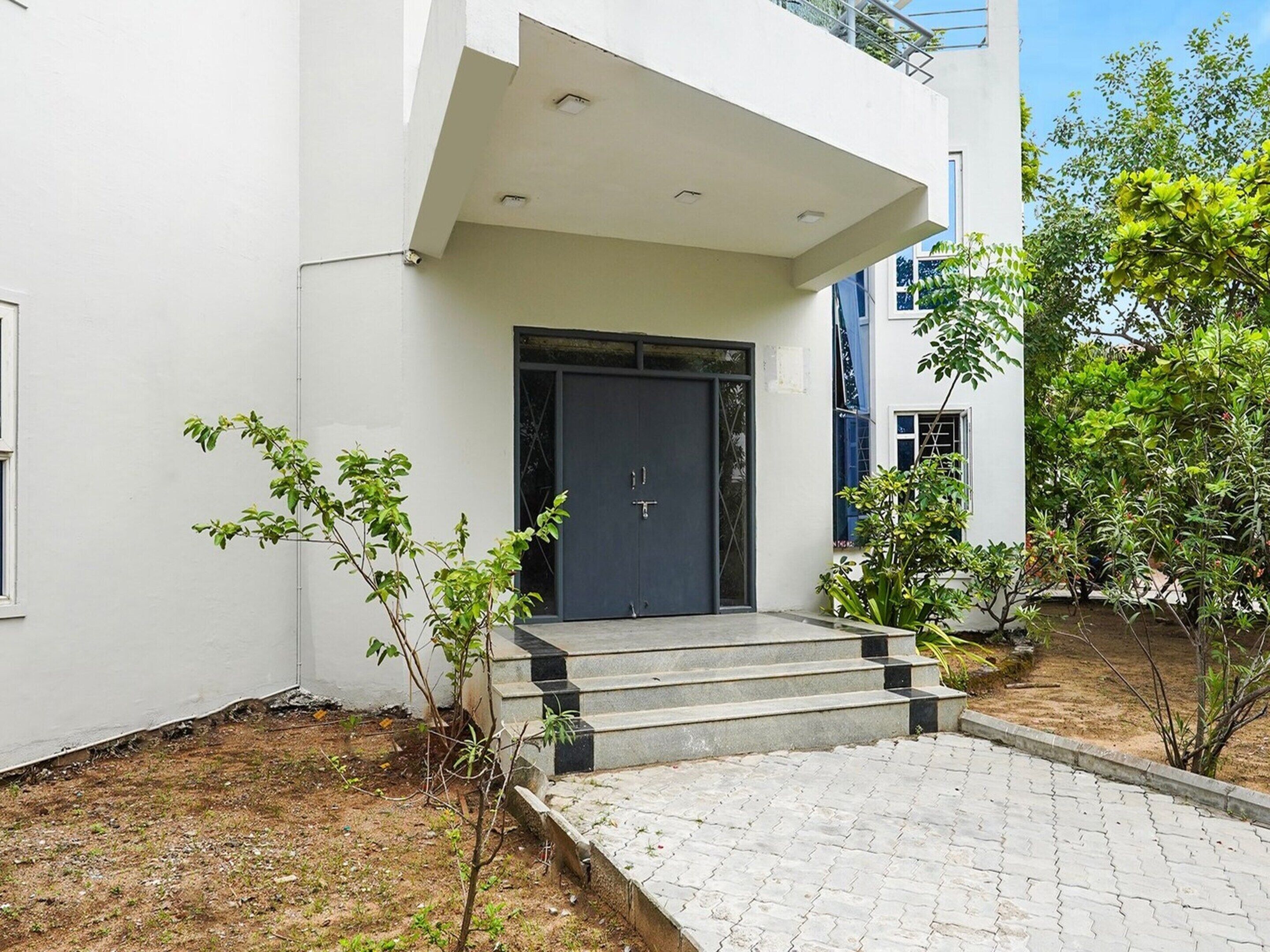 A modern building with a dark entrance door, a small set of steps leading up to the door, and a paved area in front.