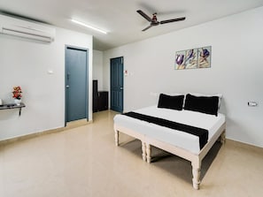 Une chambre à coucher comprenant un lit, un ventilateur de plafond, un climatiseur fixé au mur et une porte donnant sur une autre pièce.