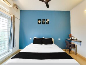 A bedroom with a bed, a desk with a chair, a ceiling fan, and a window with curtains.
