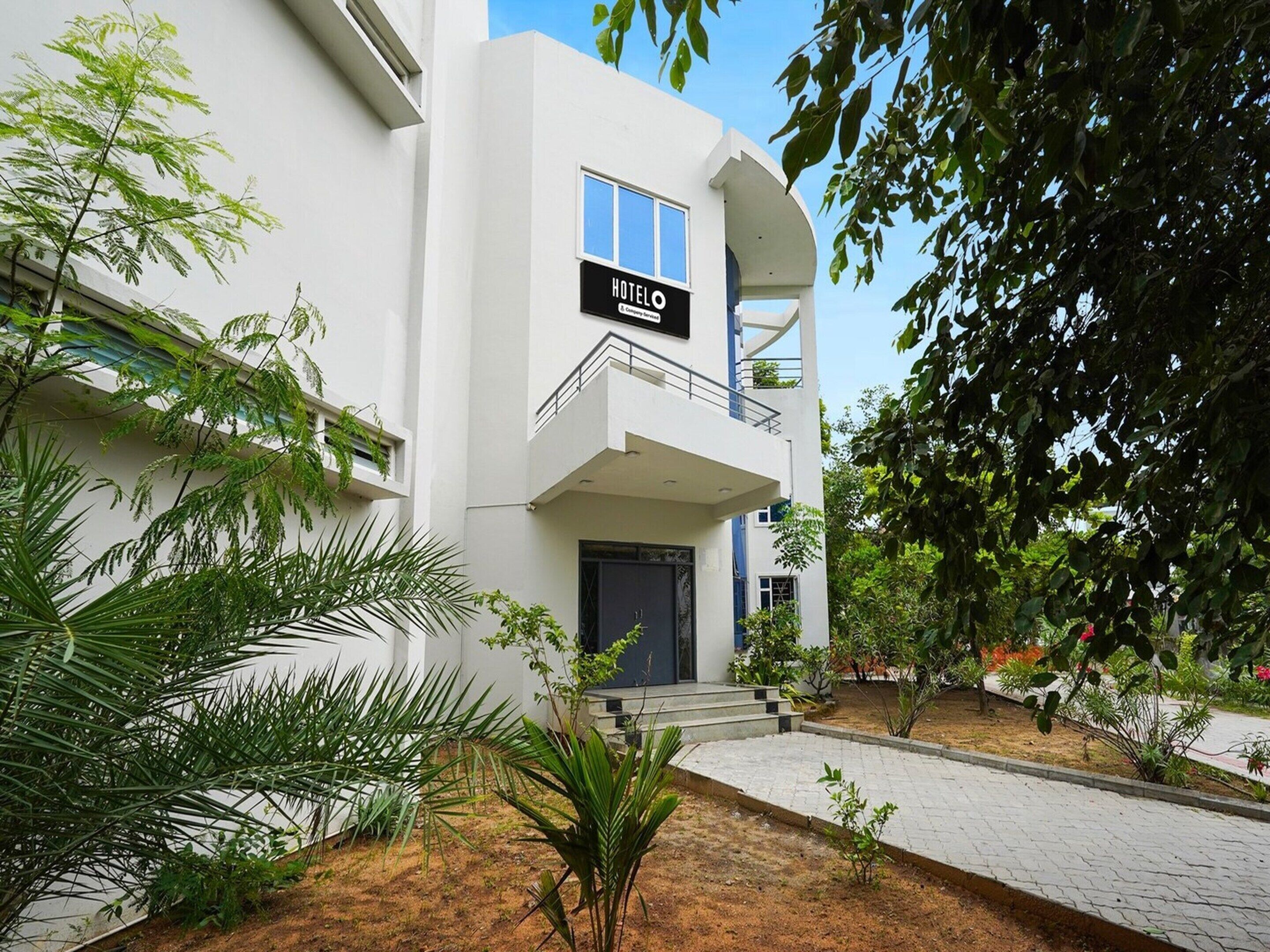 A modern hotel with a sign reading 'HOTEL,' a balcony, and a paved entrance area with plants.