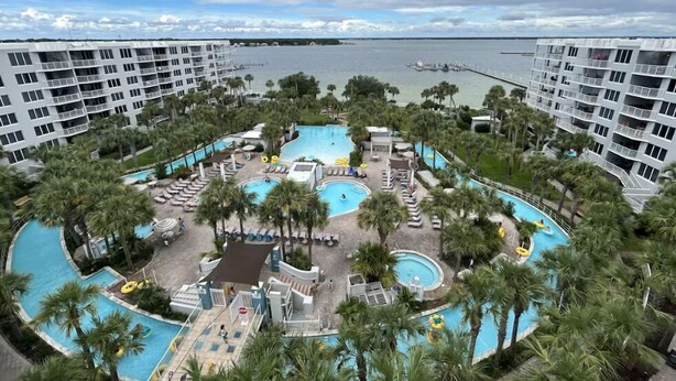 Ein Resort mit mehreren Schwimmbecken, Palmen und einem Hafen im Hintergrund.