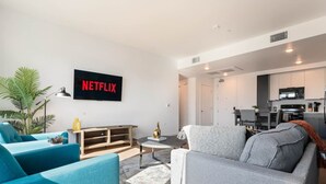 Ein modernes Wohnzimmer mit Flachbildfernseher, zwei Sofas, einem Couchtisch und einer Küche im Hintergrund.