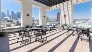 Eine Dachterrasse mit Sitzgelegenheiten im Freien, großen Fenstern und Blick auf die Stadt.