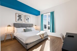 Una camera d'albergo moderna con un letto, lampade sui comodini, una scrivania e una finestra con tende.